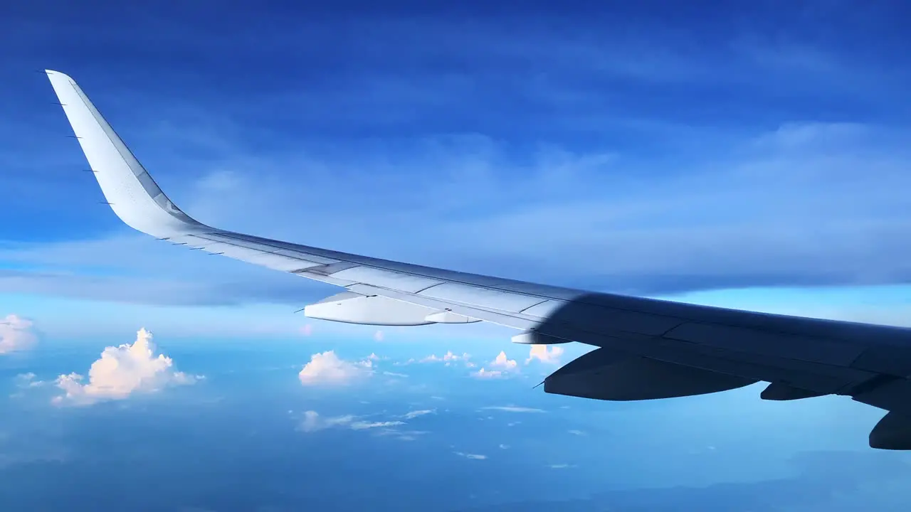 Footage of a flying Airplane into the blue cloudy sky showing the left wing