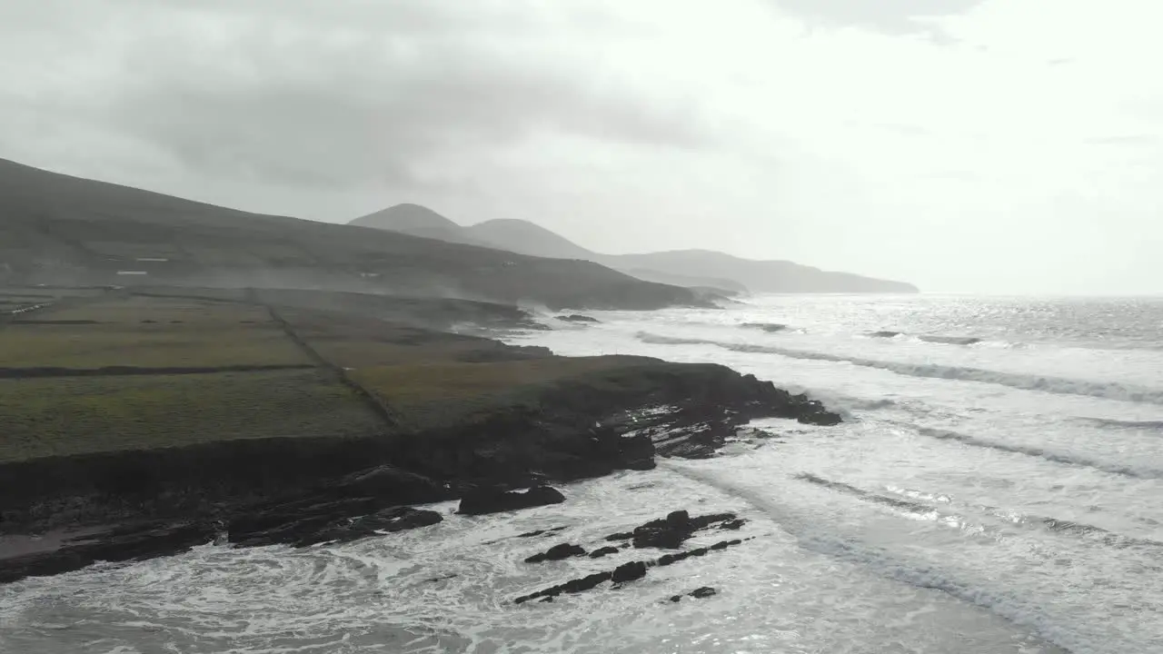 Aerial of rising drone above rugged irish coastline with waves and white spray