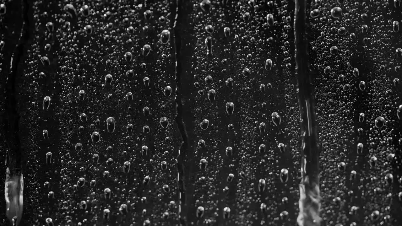 Close up rain on window Water Drops following down on black background