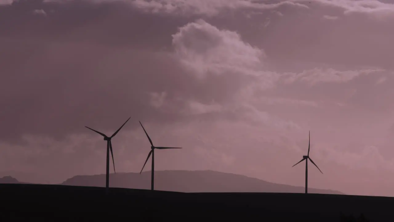 Silhouetted turning wind turbines against a cloudy and moody sky