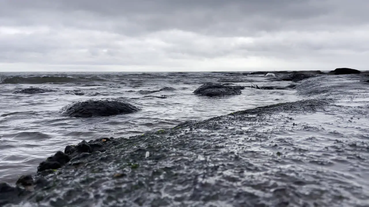 Shot looking across a rock pool with the water slashing up over the rocks on a grey and cloudy day