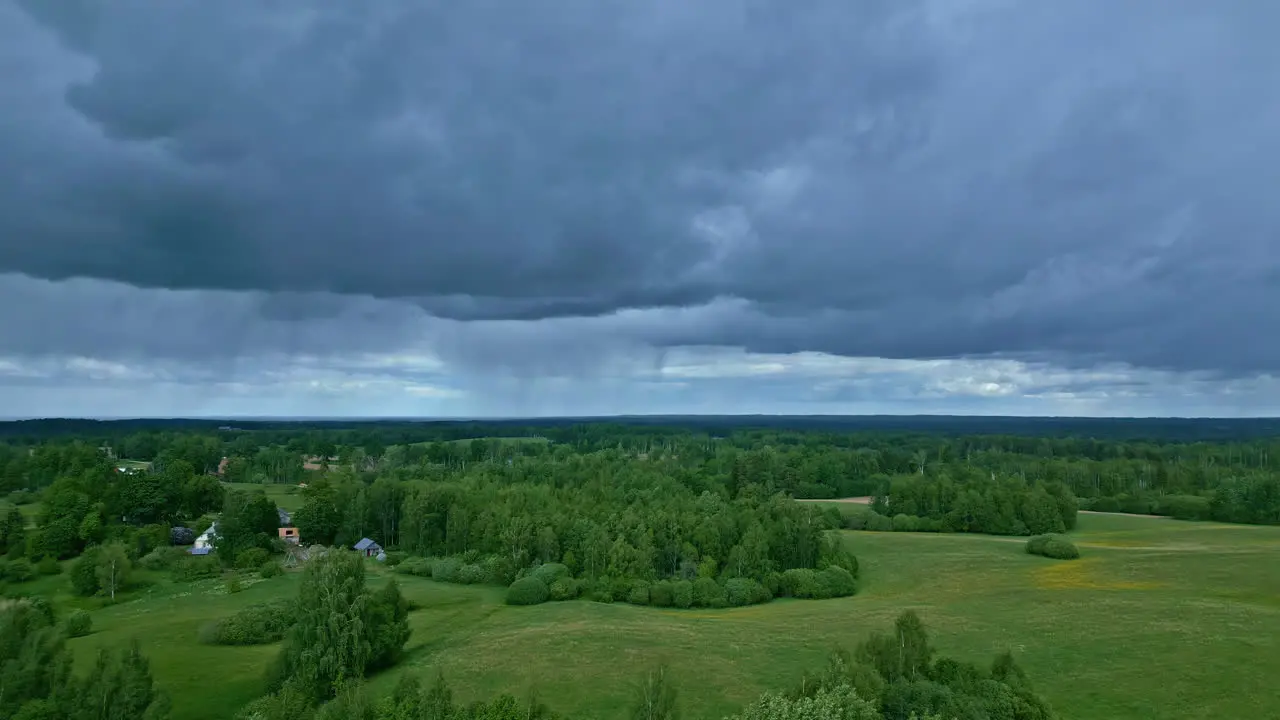 Ominous Dark Blue Clouds Slowly Moving Over Lush Green Fields with Trees Below in a Dramatic Landscape