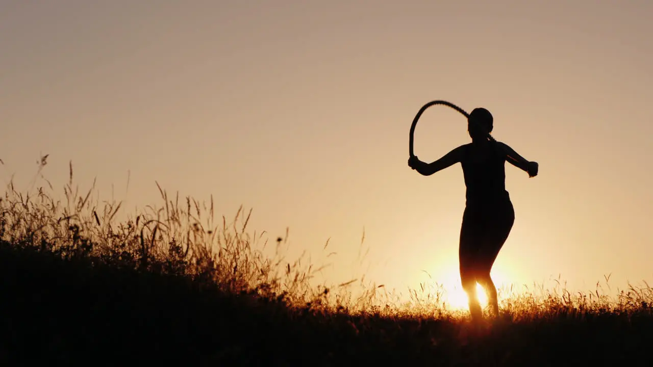 Training In The Fresh Air A Silhouette Of A Woman Jumping Over A Rope At Sunset