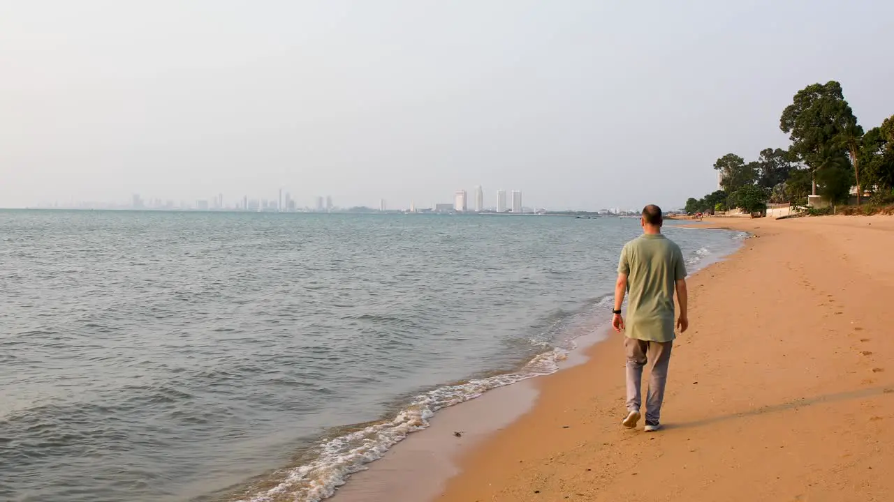 Male Tourist Walking Away Along the Beach of Bangsaray in Pattaya Thailand with City View in the Distance