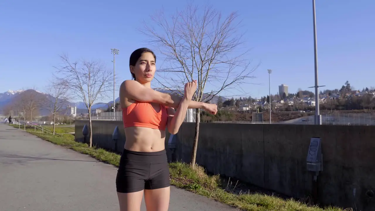 Young woman stretching arms and shaking muscles before outdoor workout