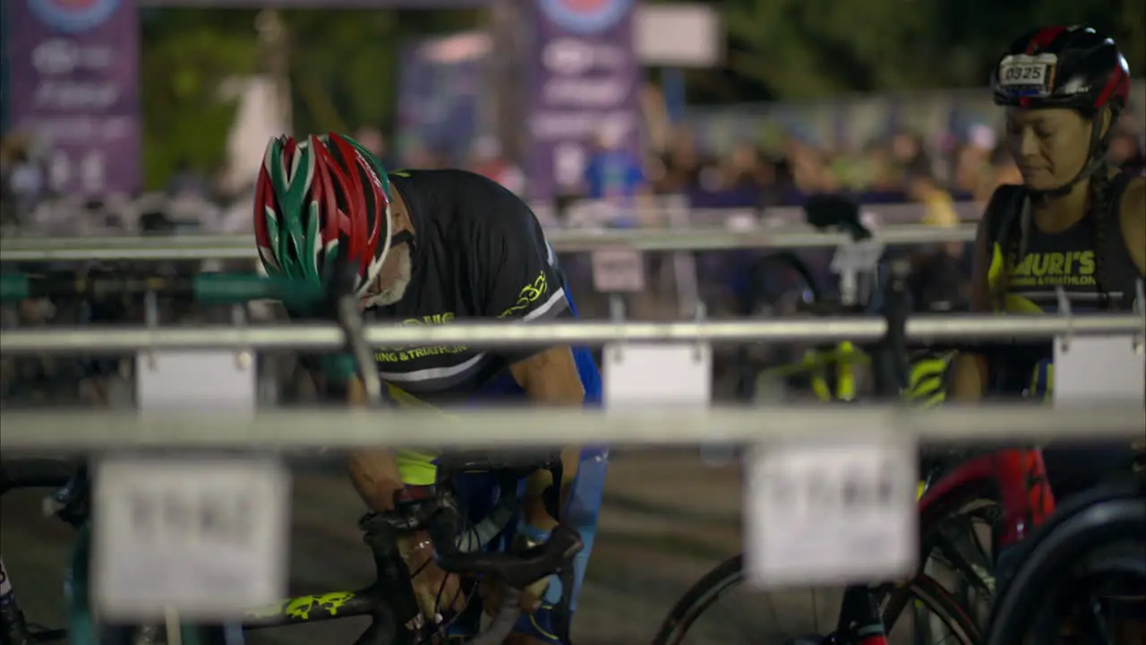 Senior male athlete wearing a helmet pumping air into his bike's wheel early in the morning before the competition starts