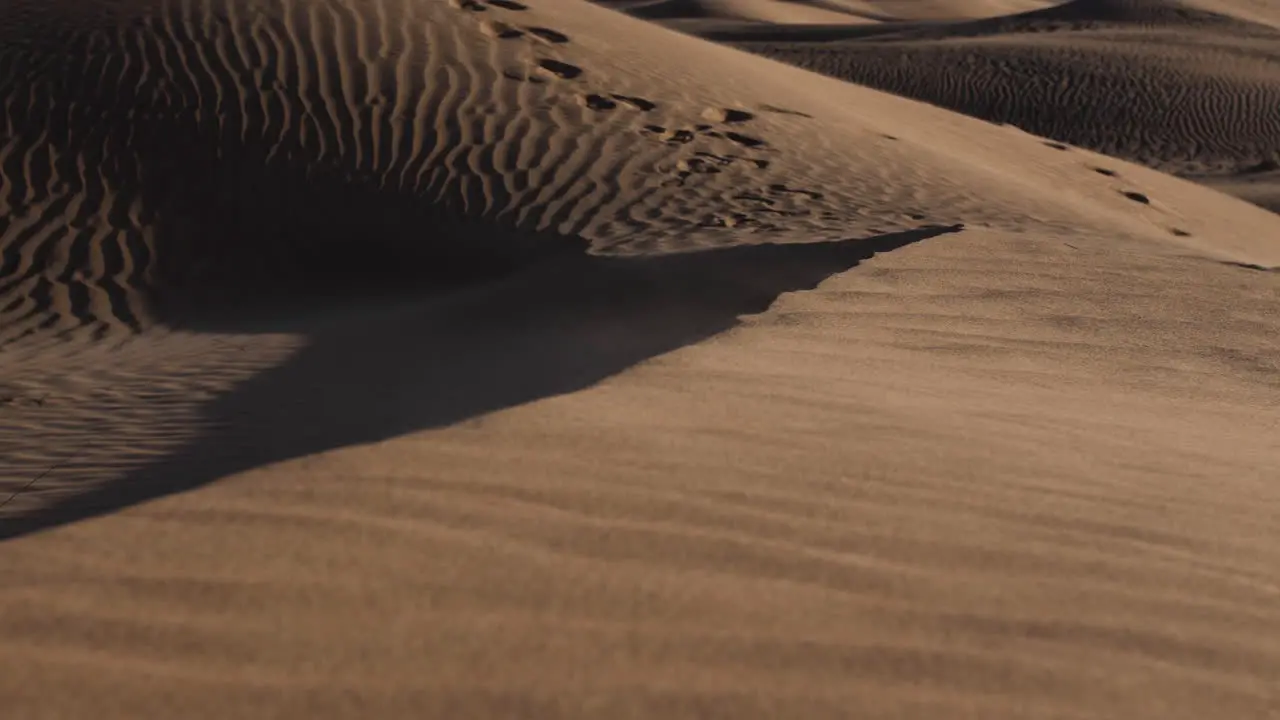 Sand blowing over sand dunes with distant footprints in middle eastern desert landscape near Dubai in the United Arab Emirates