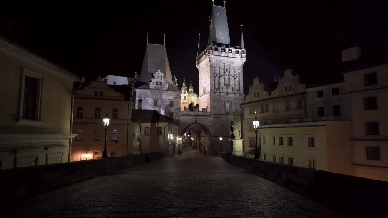 A view of a gothic gate tower at one end of Charles bridge in the historical city centre of Prague at night during a Covid-19 lockdown with no people anywhere picturesque architecture tilt 4k shot