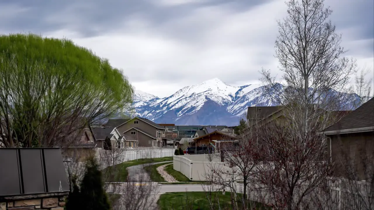 Time lapse on an overcast day of a cloudscape blowing over the snow-capped mountains beyond a housing suburb