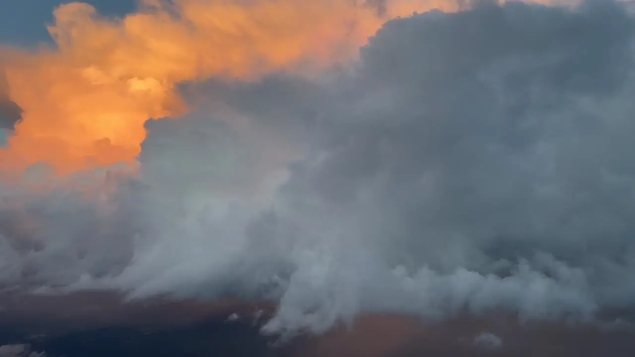 Aerial view from a jet cockpit of a huge cumulonimbus iluminated with orange color in the afternoon at 35