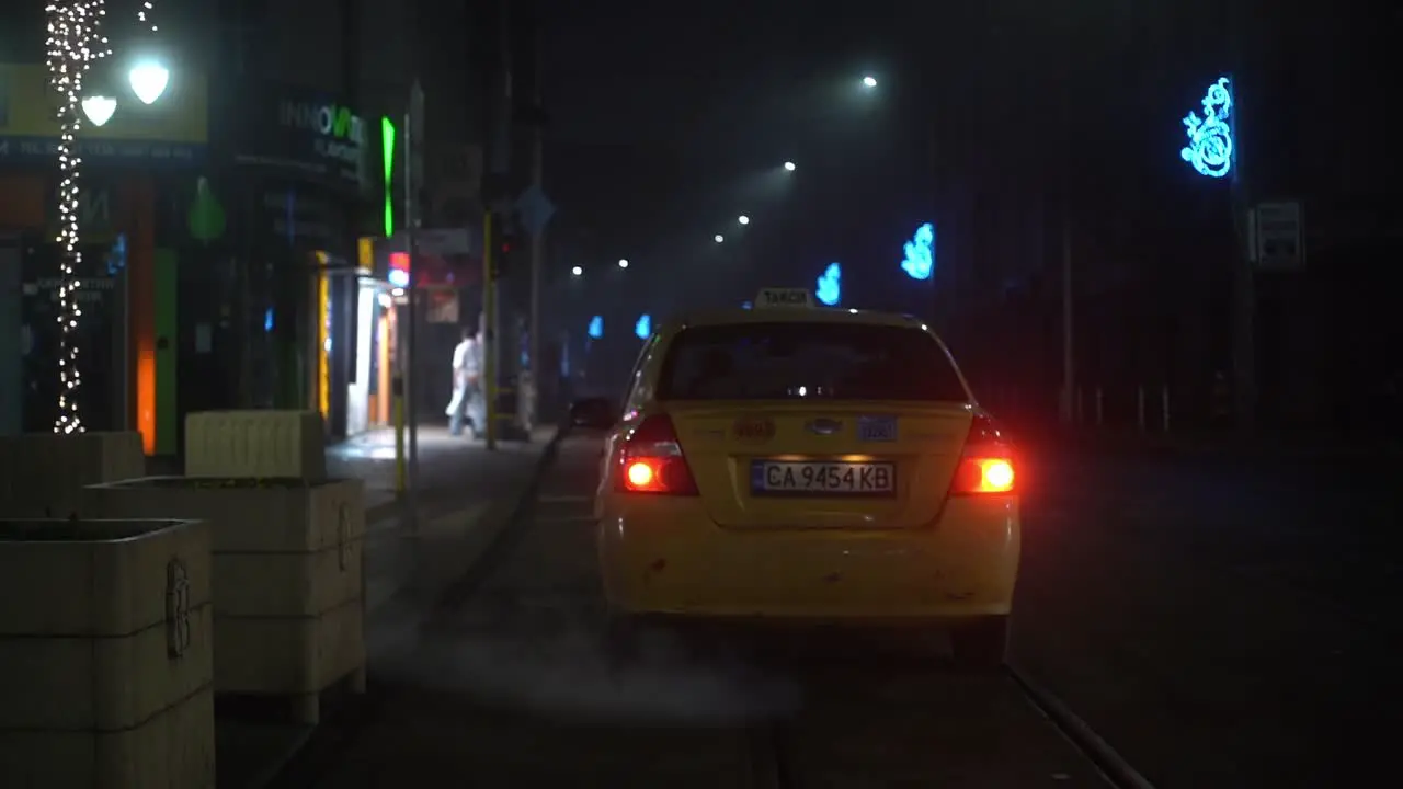 Taxi cab idles outside of empty restaurant and shops at night time