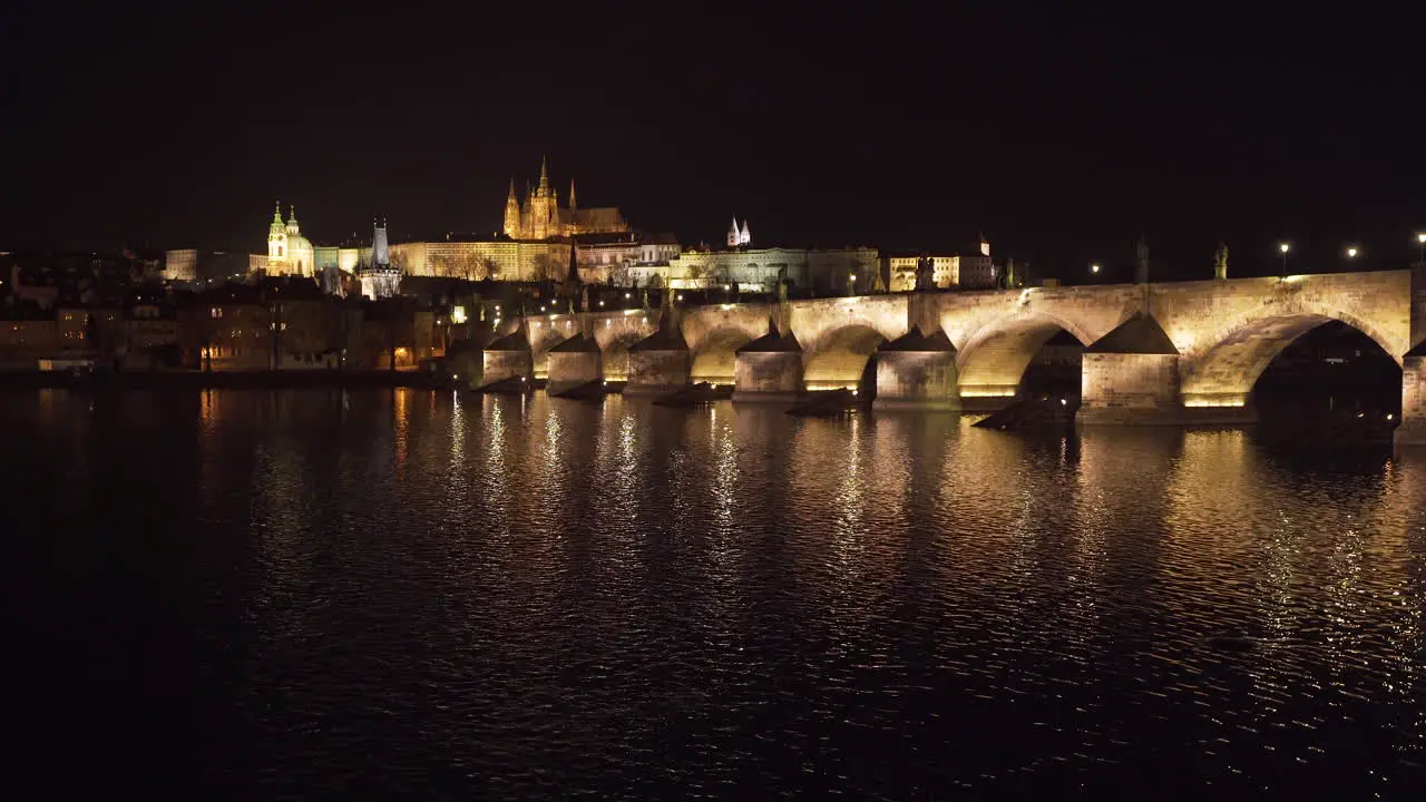 The Prague Castle and Charles bridge over river Vltava in the historical centre of Prague Czechia lit by lights at night shot from the other side of the river water slowly flowing below the bridge