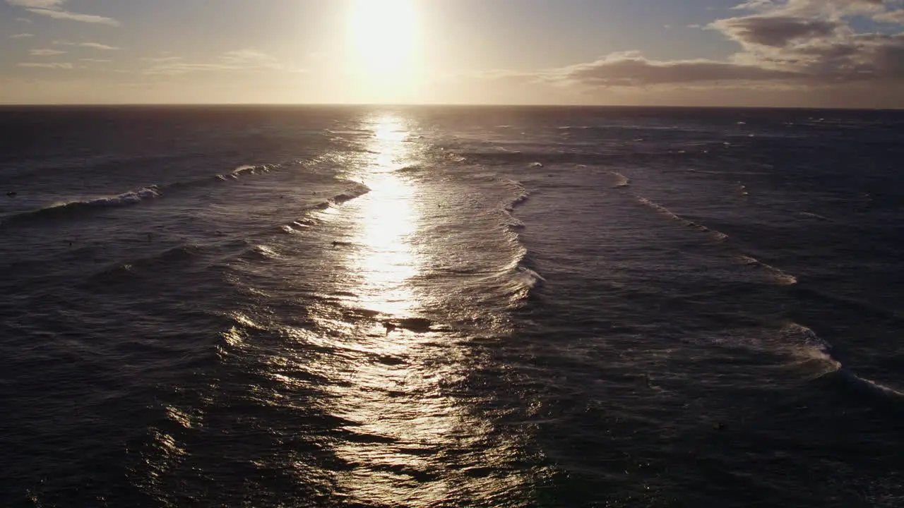 aerial footage of the golden refection of the sun setting on the Pacific ocean as the waves travel horizontally to the shore