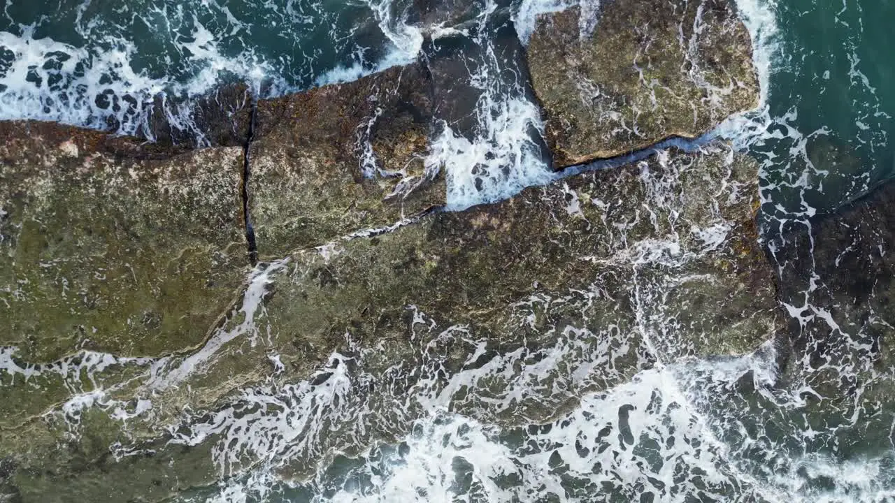 Top down view of strong ocean waves crashing on flat algae covered rocks white water