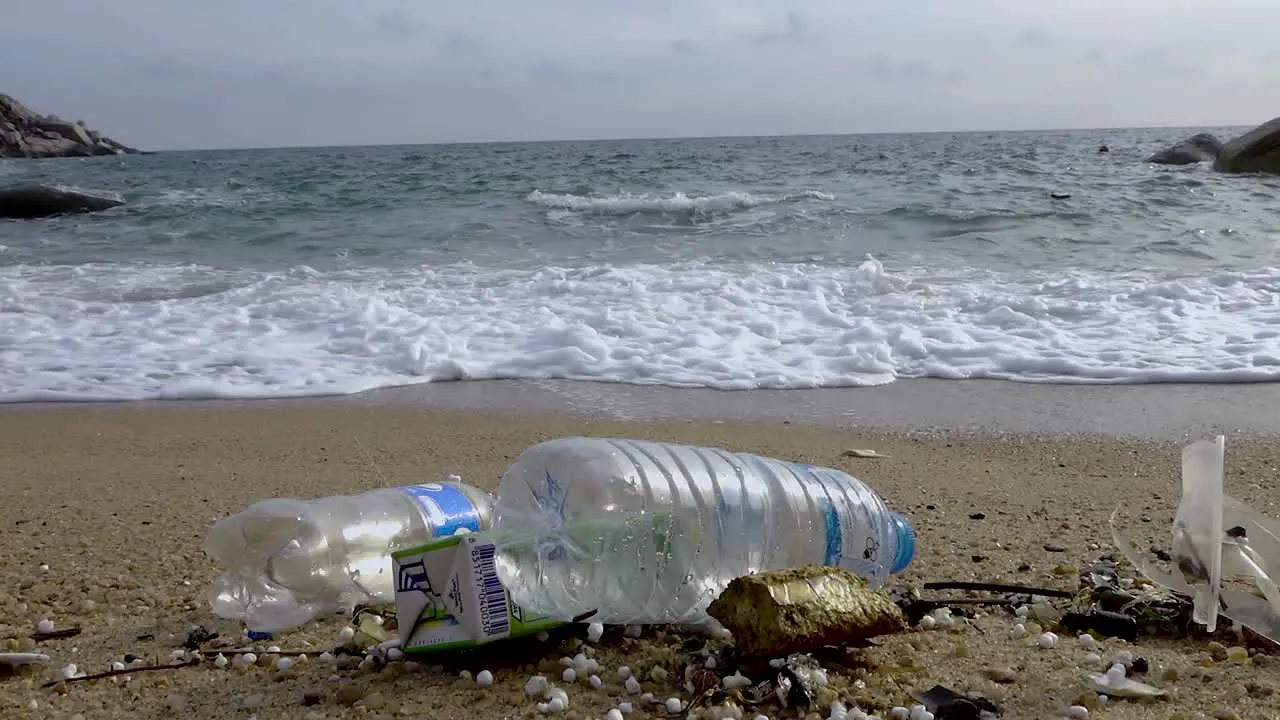 Littered plastic bottles littered in beachfront near rushing wave slow zoom in steady shot