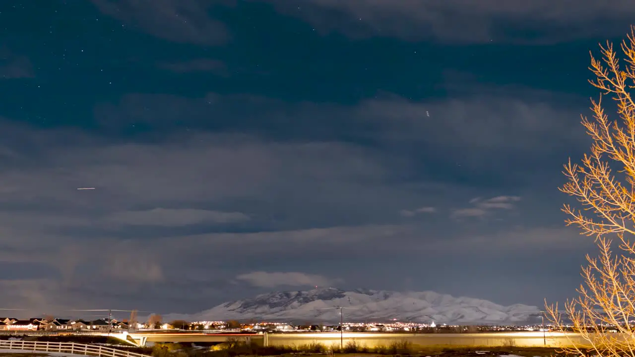 Stars crossing the sky as a winter snowstorm blows in nighttime time lapse over a suburban landscape