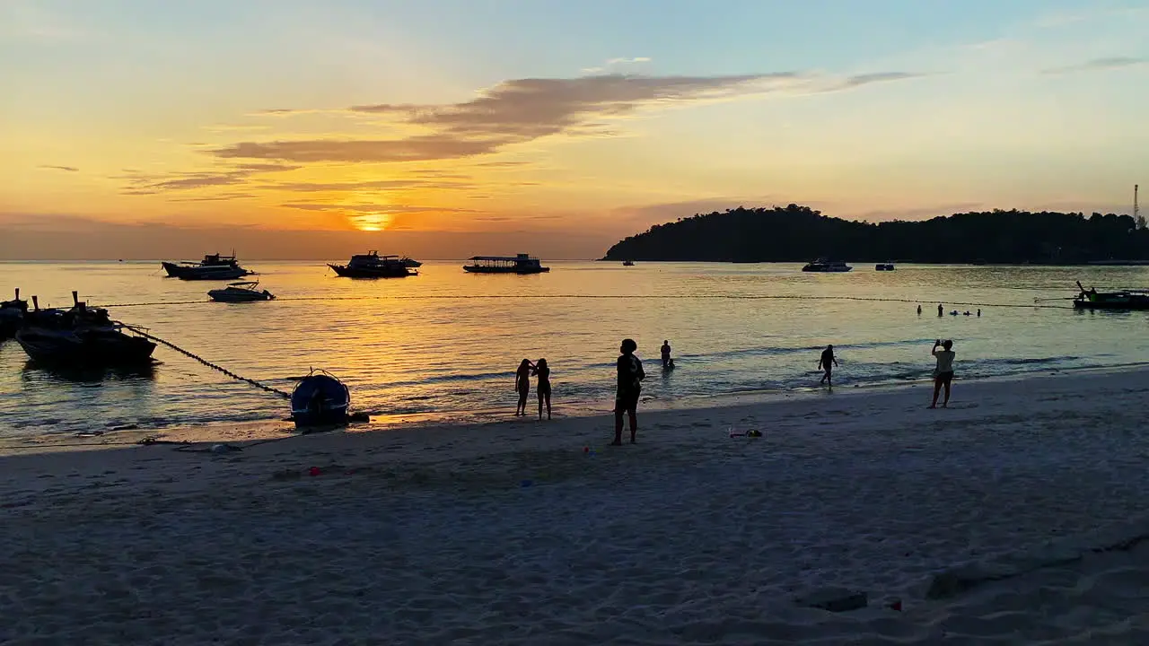 Wide Time Lapse shot of a beach line and silhouette of people playing with an ocean and orange color sunset in the background