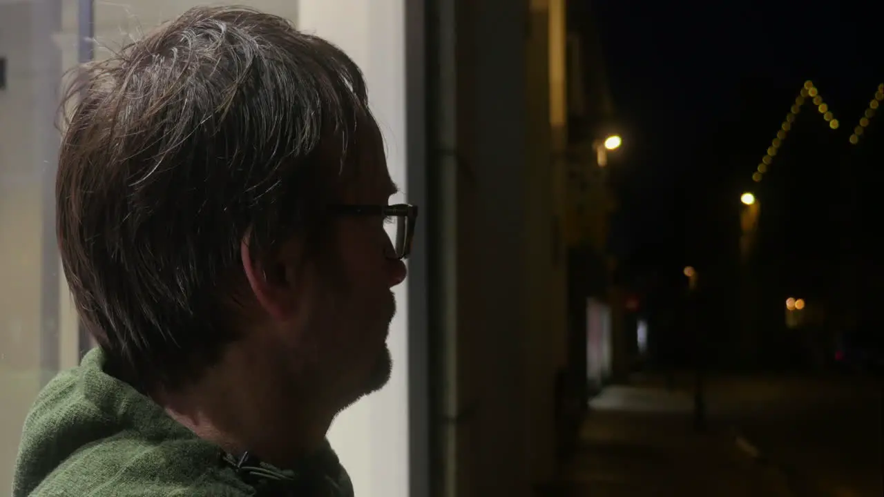 Caucasian man waiting outside quiet street shop window in the late cold night air side view