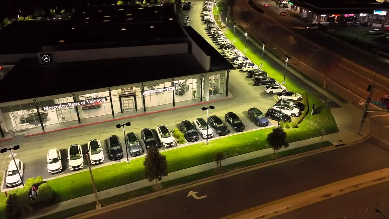 Illuminated Mercedes Benz car dealership Valencia California night time aerial view rising above luxury showroom