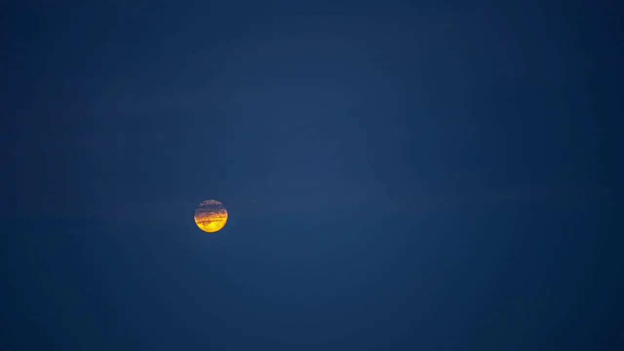 Low angle shot of full moon rising in the night sky over dark clouds in timelapse