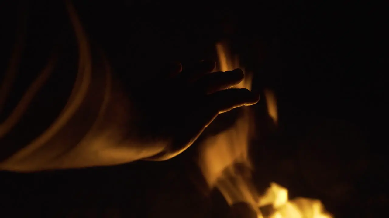 In the darkness of the night someone warms their hand by gently rotating it in front of a burning fire