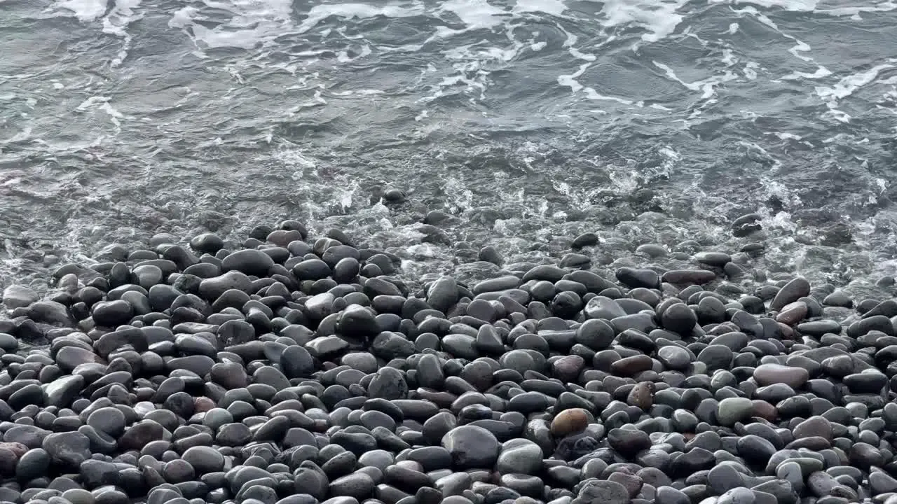 Sea water waves into rocky pebble stone beach relaxing calming in Tenerife