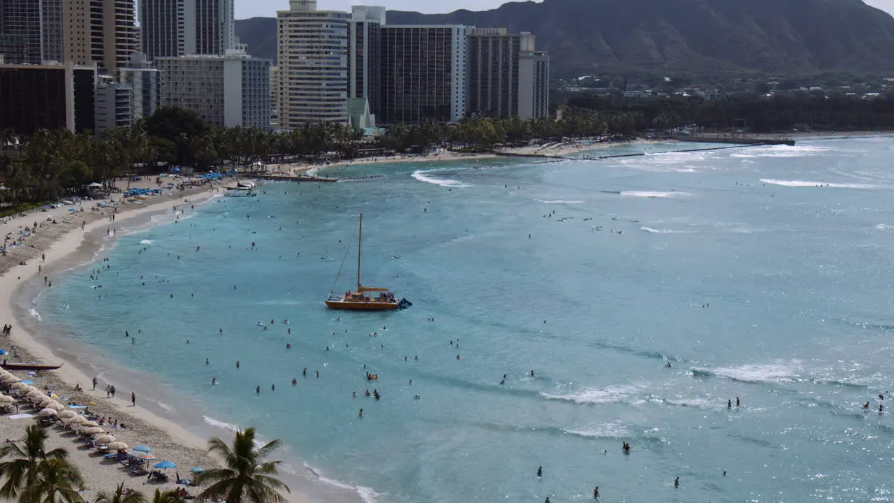 Yellow Catamaran Setting Sail against Waves Surrounded by crowds of Beachgoers Hawaii Wide Shot