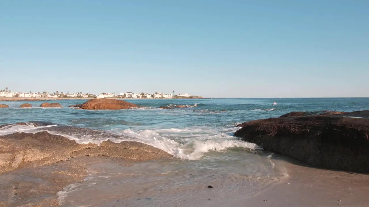 View of ocean waves breaking on rocks in the foreground with houses in the distance