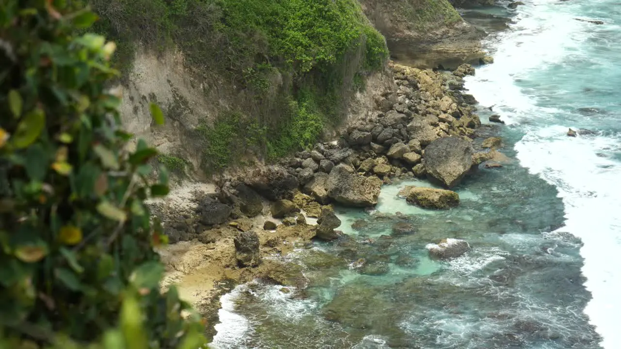 Slow-motion close up of waves breaking on shore below from cliff in Uluwatu Bali