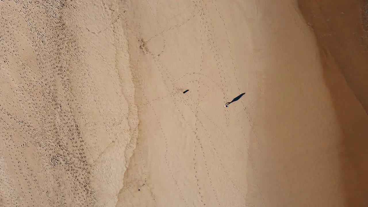 Bird's-eye aerial of an individual strolling along a sun-kissed sandy beach rhythmic dance of sea waves caresses the shoreline