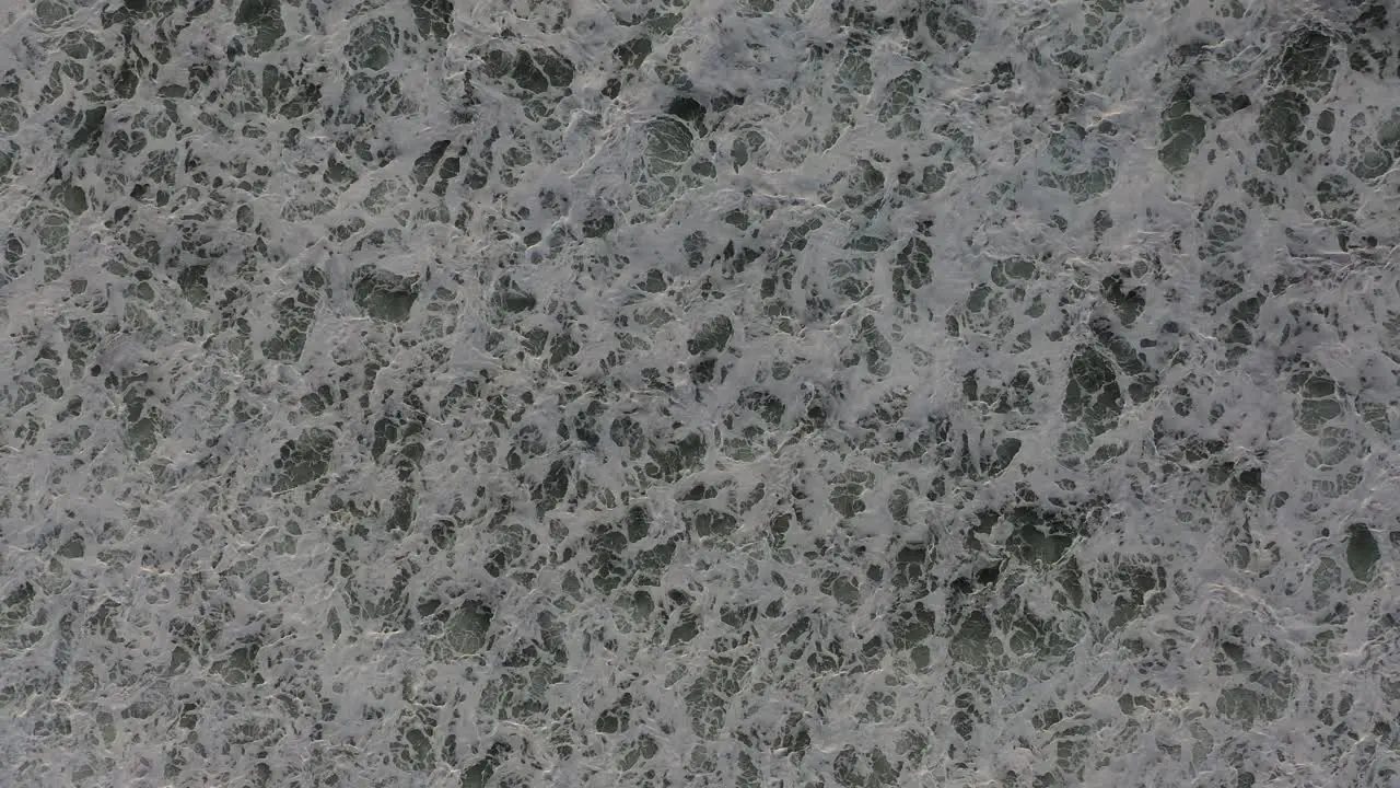 A mesmerizing drone shot of white water after a wave crash showcasing the intricate patterns of the waves as the drone ascends capturing the raw power of the ocean