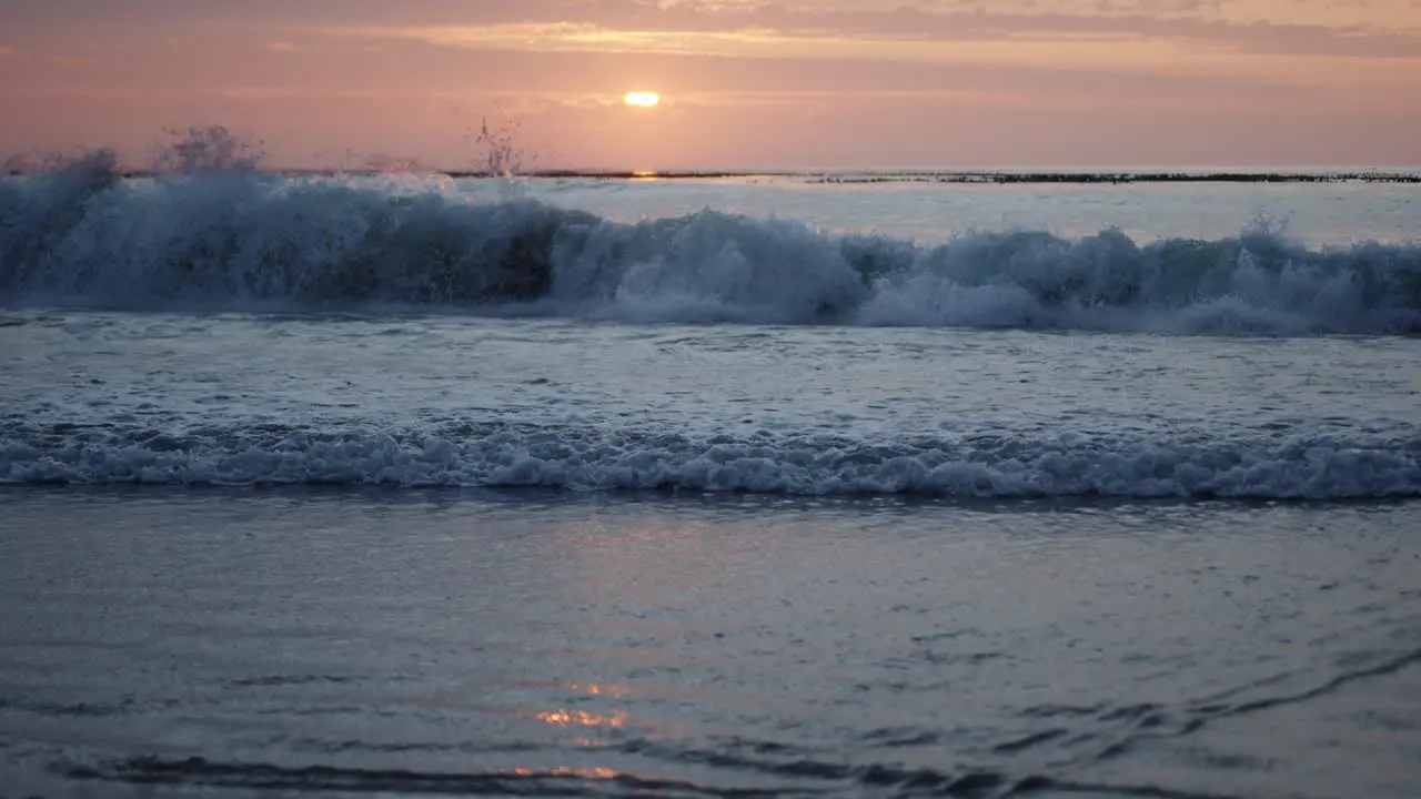 Sunrise reflecting on the water as a wave comes crashing down in slow-motion