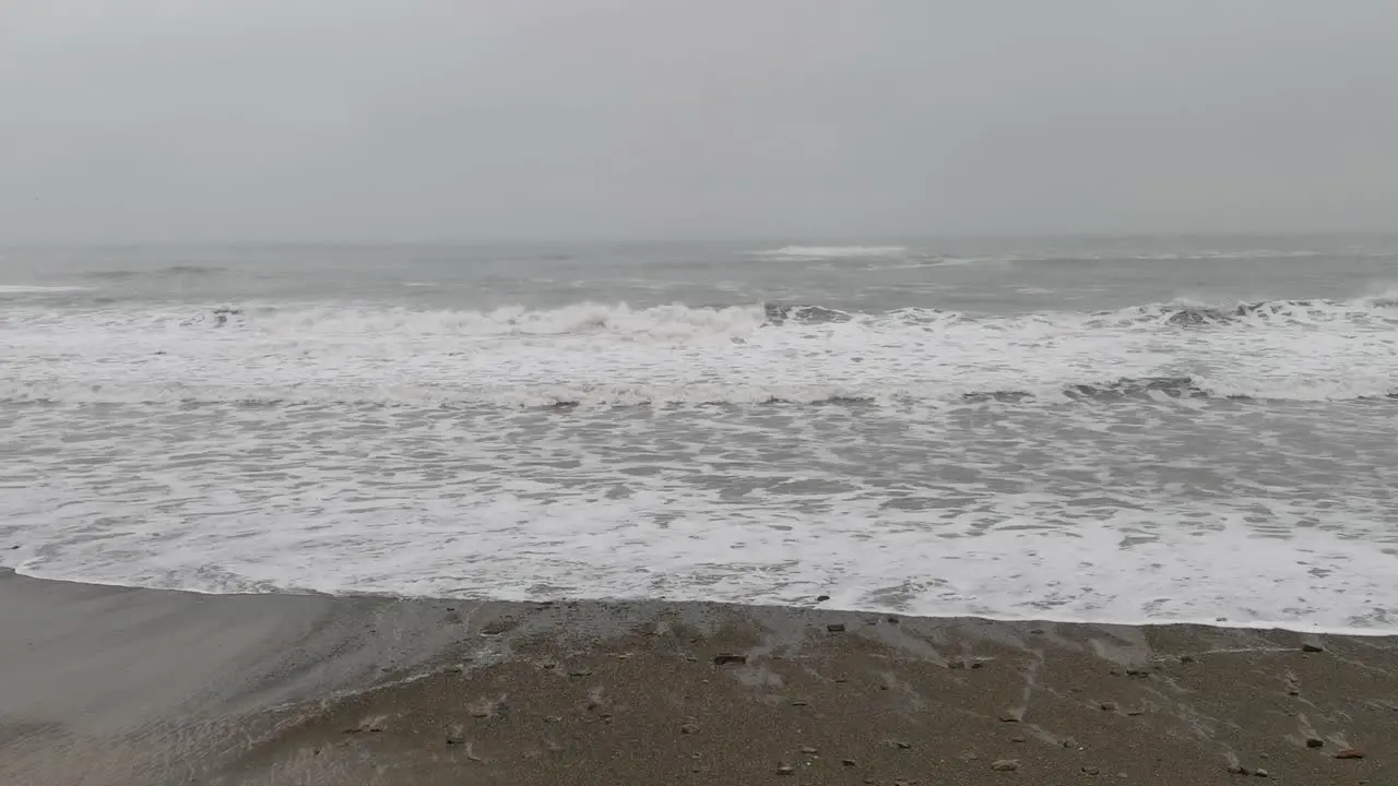 Movement of waves on a ocean sore with stormy weather mist covering sky