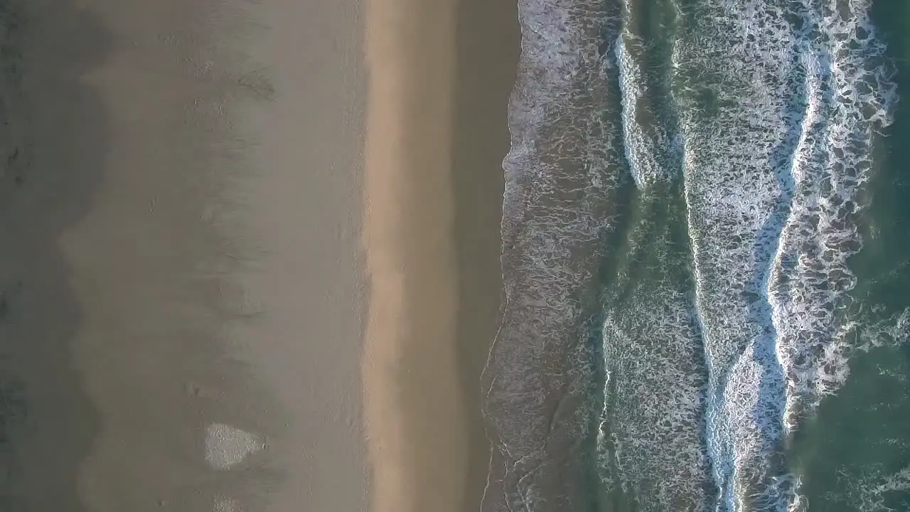 Aerial drone shot looking down symmetrically aligned with beach shore and sea waves crashing