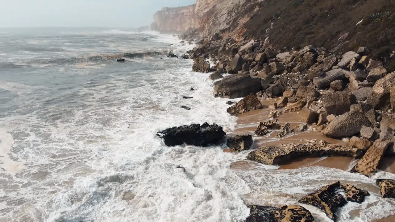 Aerial footage capturing the unyielding force of sea waves crashing against the rugged coastal expanse of Nazare Portugal