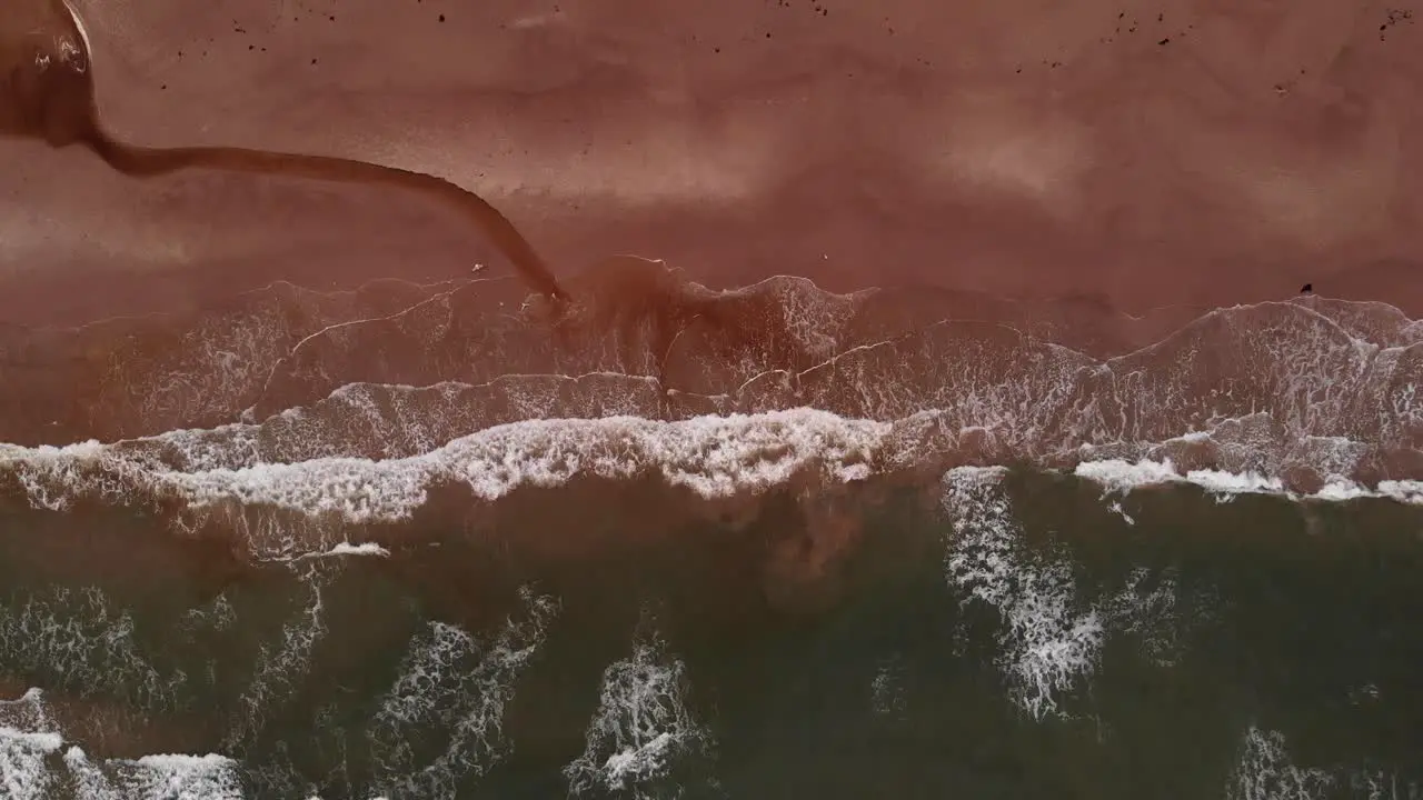 Aerial top down view of empty and lonely orange sand beach with long white waves and a small spring leading into the ocean