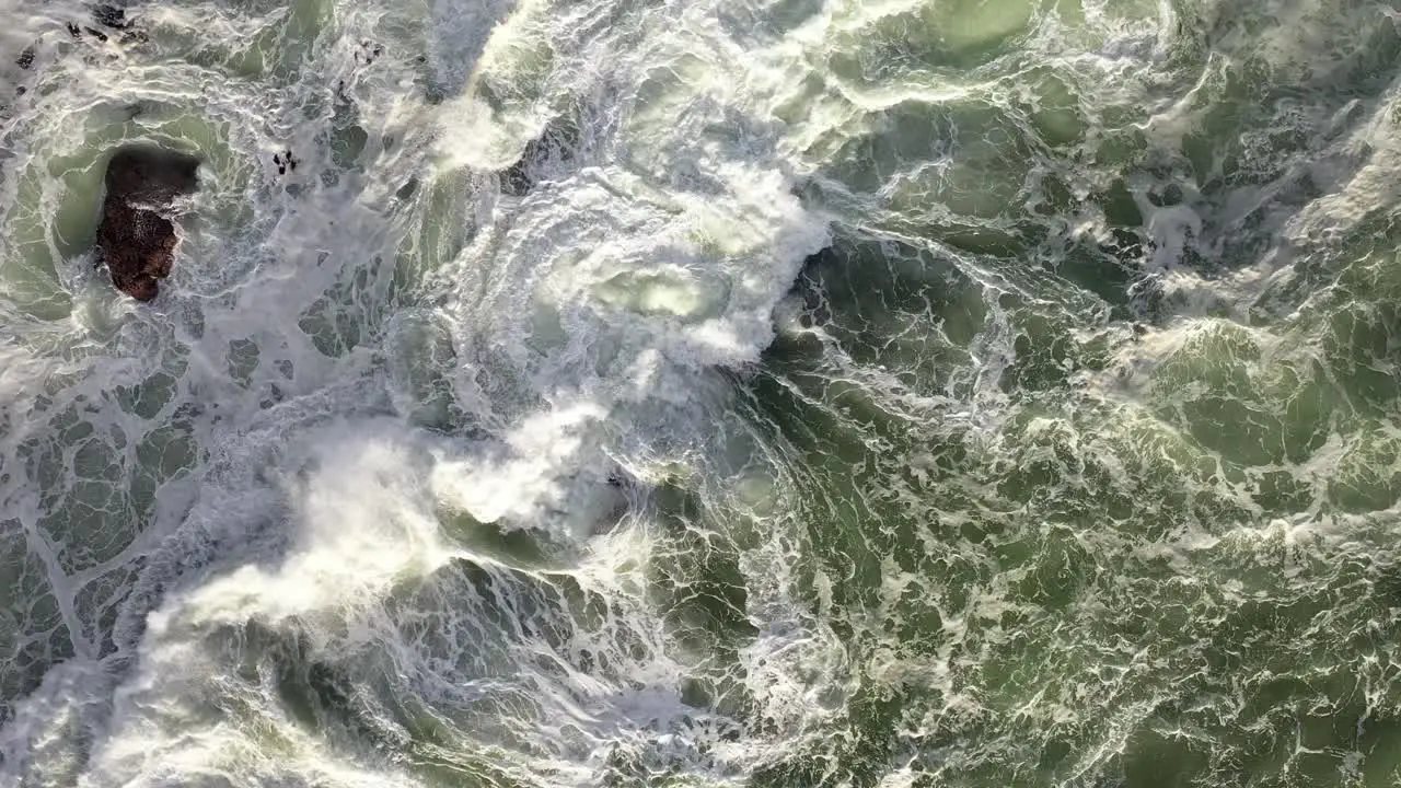 Cinematic Cenital Static Shot of Rough Ocean Waves Hitting Rocks During Sunset at Cape Town's Camps Bay Beach