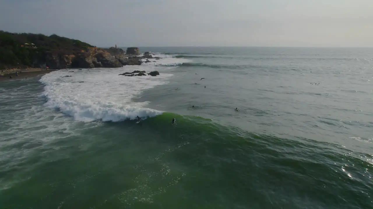 Wide drone shot of surfers trying to ride a big wave off the coast of Mexico