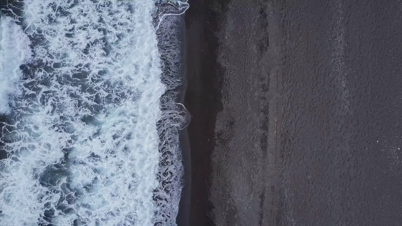 Aerial looking down at waves coming in to black sand beach in Mediterranean