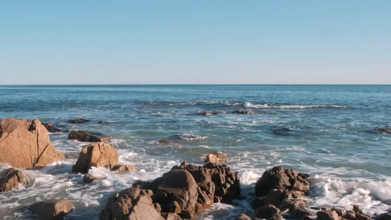 Waves softly breaking on rocks in the ocean with whale jumping in distant