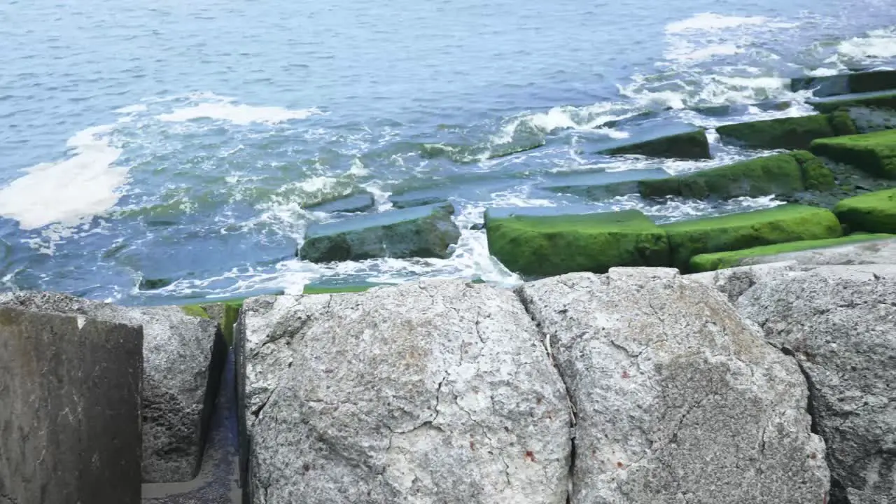 Sea waves crashing on mossy wave breaker rocks pan shot