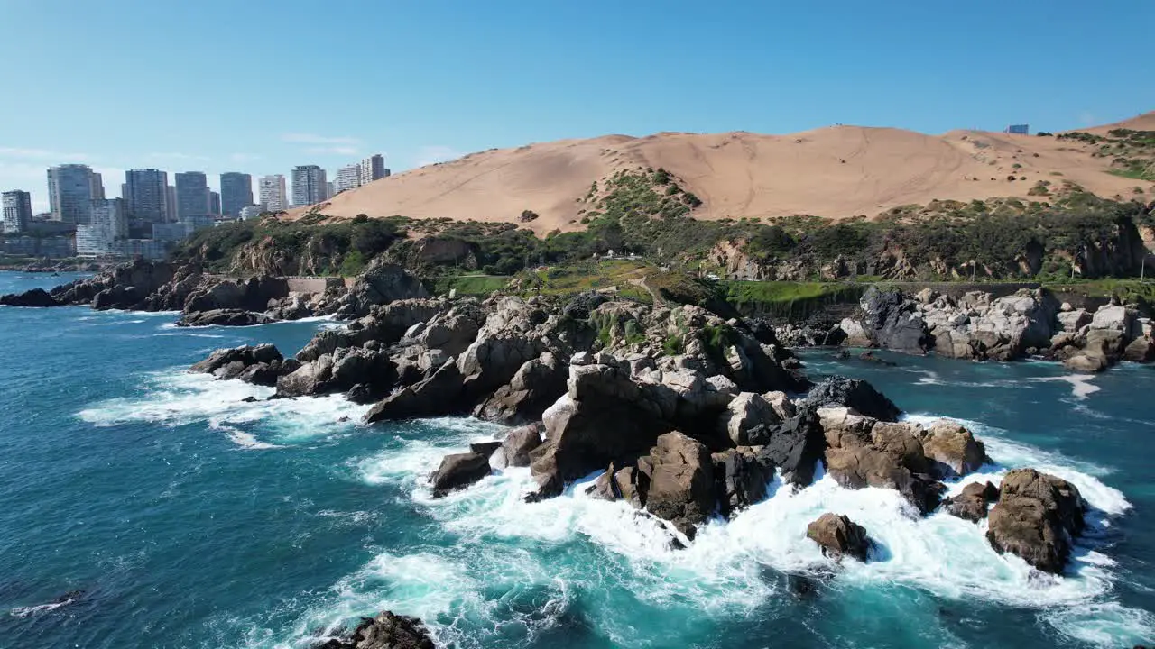 Waves Breaking on Rocks in the Coast with tall Buildings and Dunes in the background Viña del Mar Chile