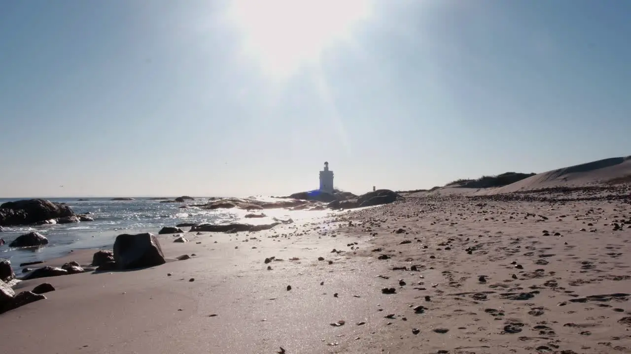 Wide angle shot of a beach scattered with small rocks and a lighthouse in the distance