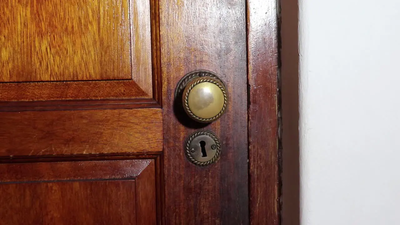 Brass Door knob turns and man with black glove opening wooden door slowly