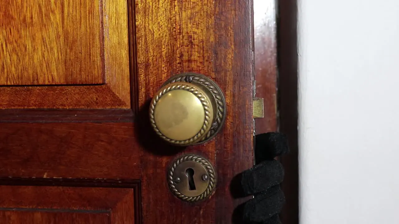 Man with a black glove slowly opens a wooden door turning the door knob and showing his hand and masked face