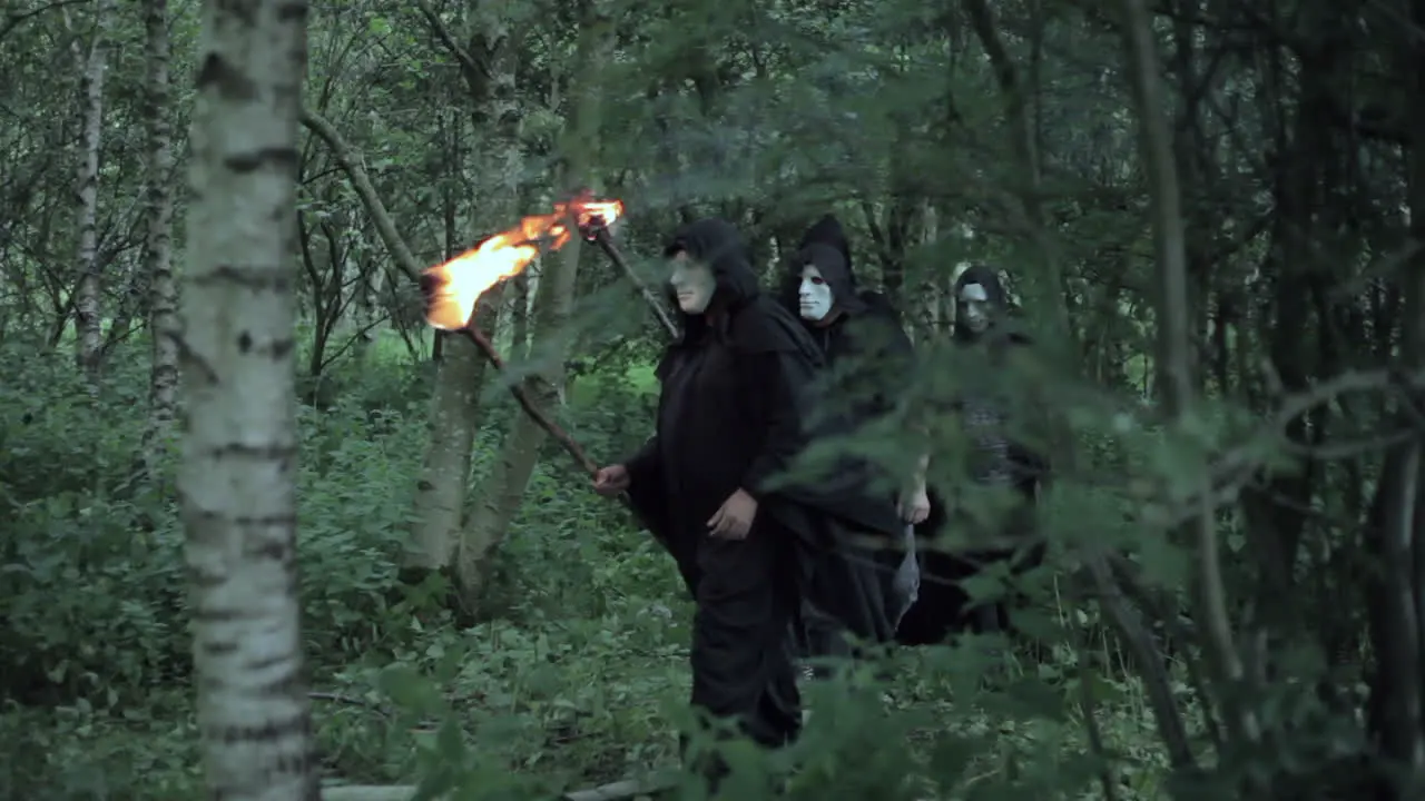 An unrecognizable man hides from a cult of evil hooded druids in the woods who are about to perform a sacrifice ritual