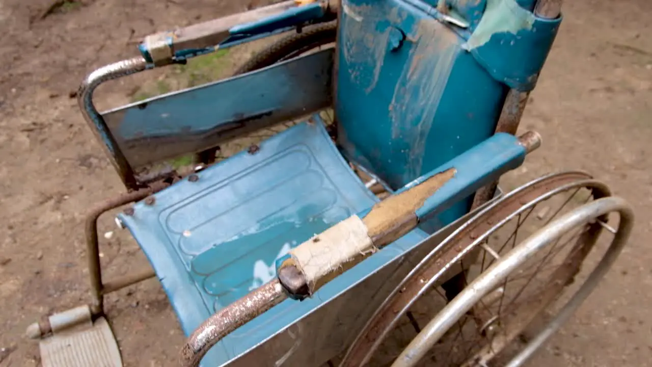 Vintage retro well-used worn and rusty wheelchair in pale blue sitting outside in the garden forest jungle