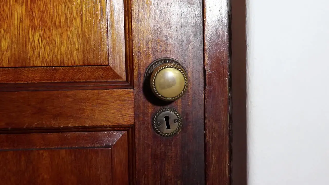 Man with a black glove on slowly opens a brass door knob on a wooden door