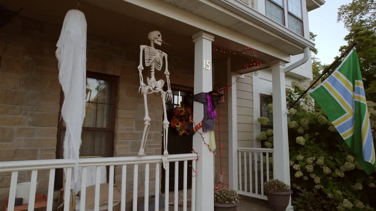 Boom down the side of a two story house in the suburbs to reveal halloween decorations on the front porch and a flag