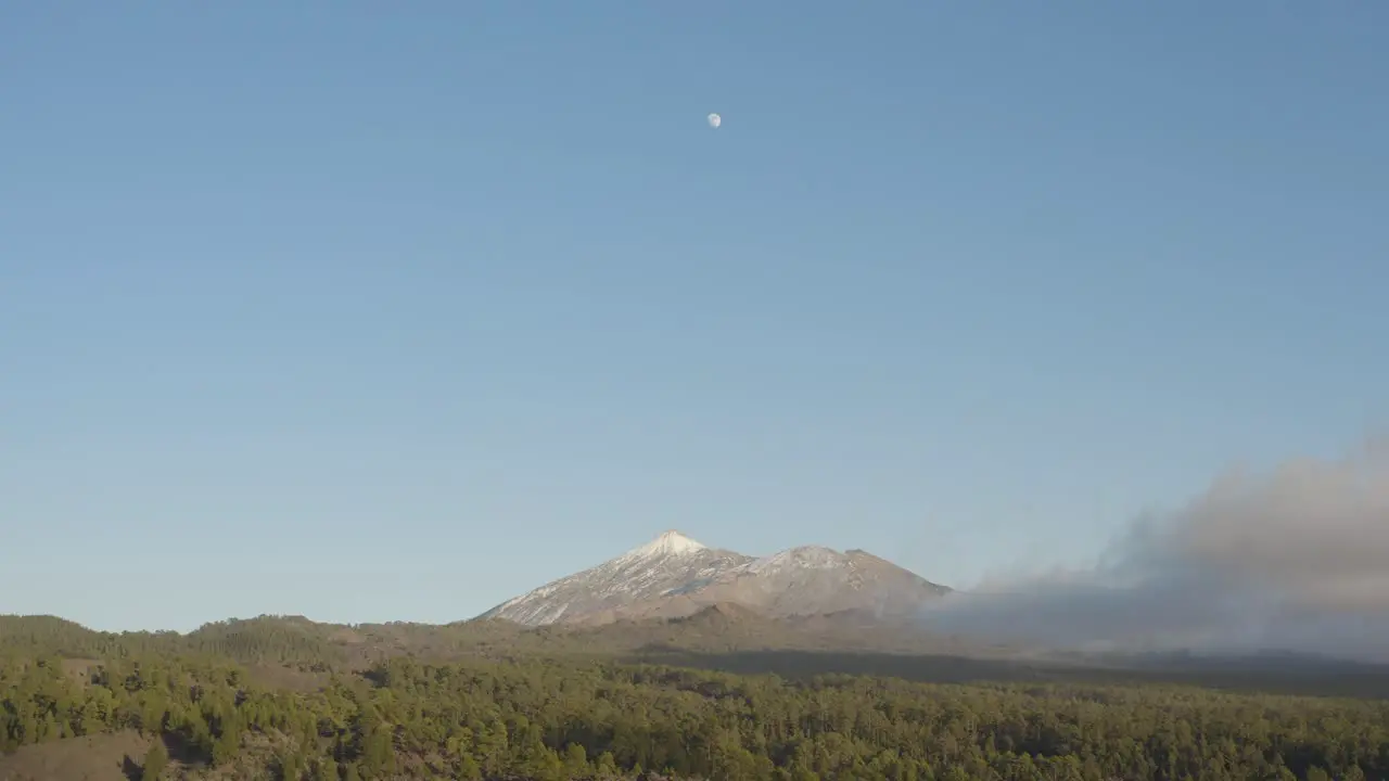 Awe inspiring view over mount Teide with moon blue sky and clouds Surrounded by green forest